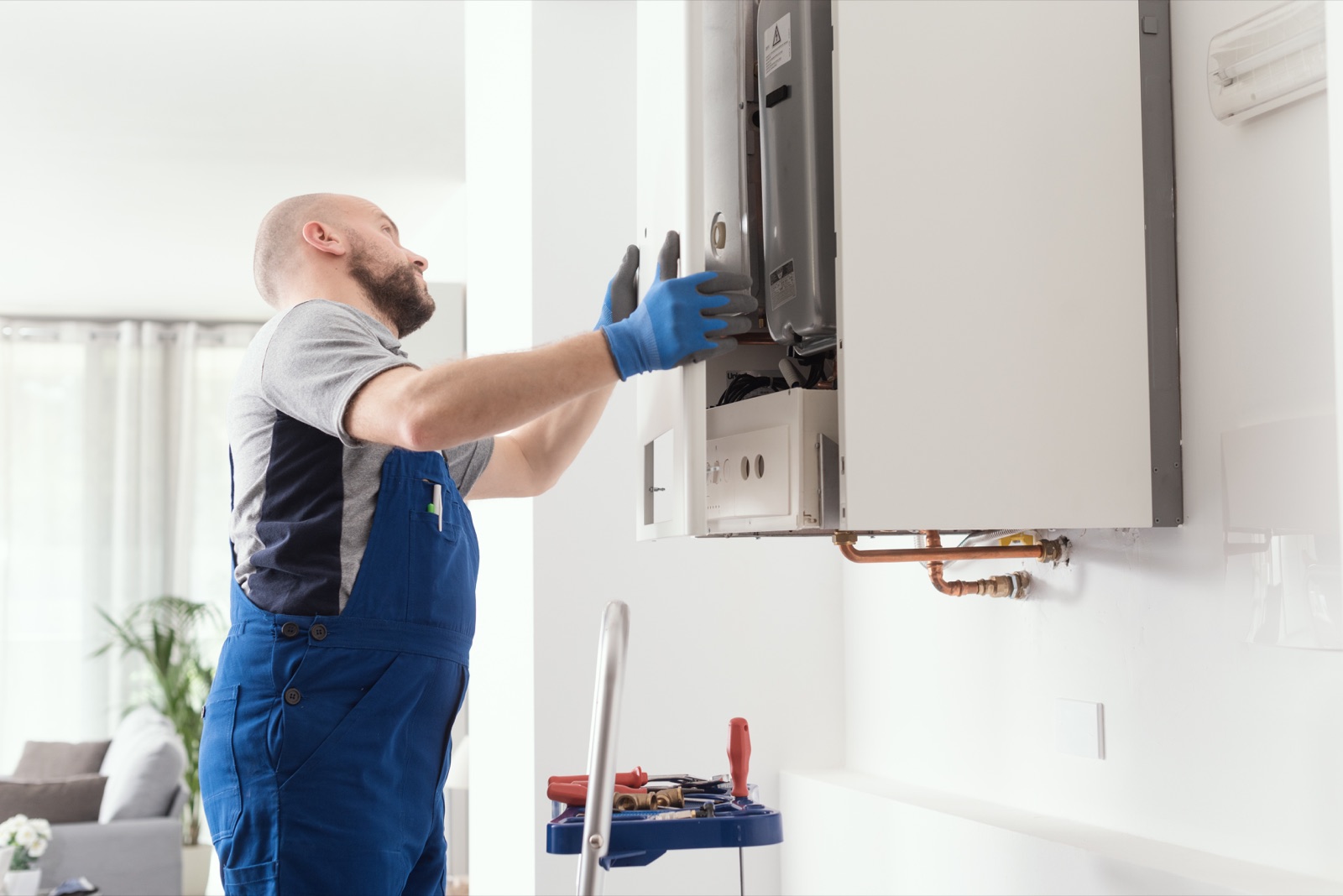 An engineer working on a wall-mounted boiler with tools
